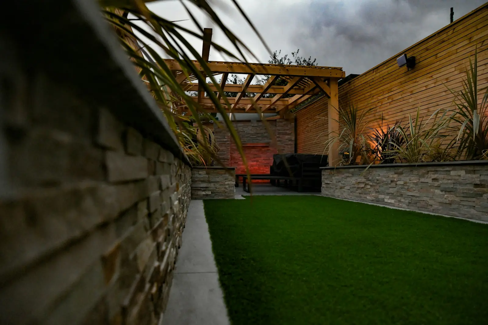 Timber pergola and stone-clad wall lit at dusk